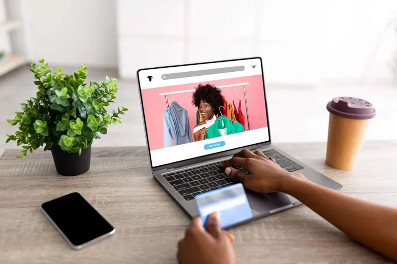 Shopper using a credit card, laptop and smartphone to buy from an e-commerce website